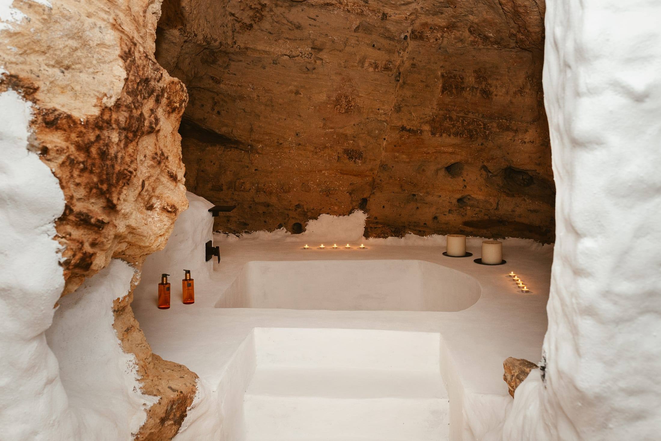 Bañera excavada en el suelo bajo una bóveda de roca, con velas encendidas