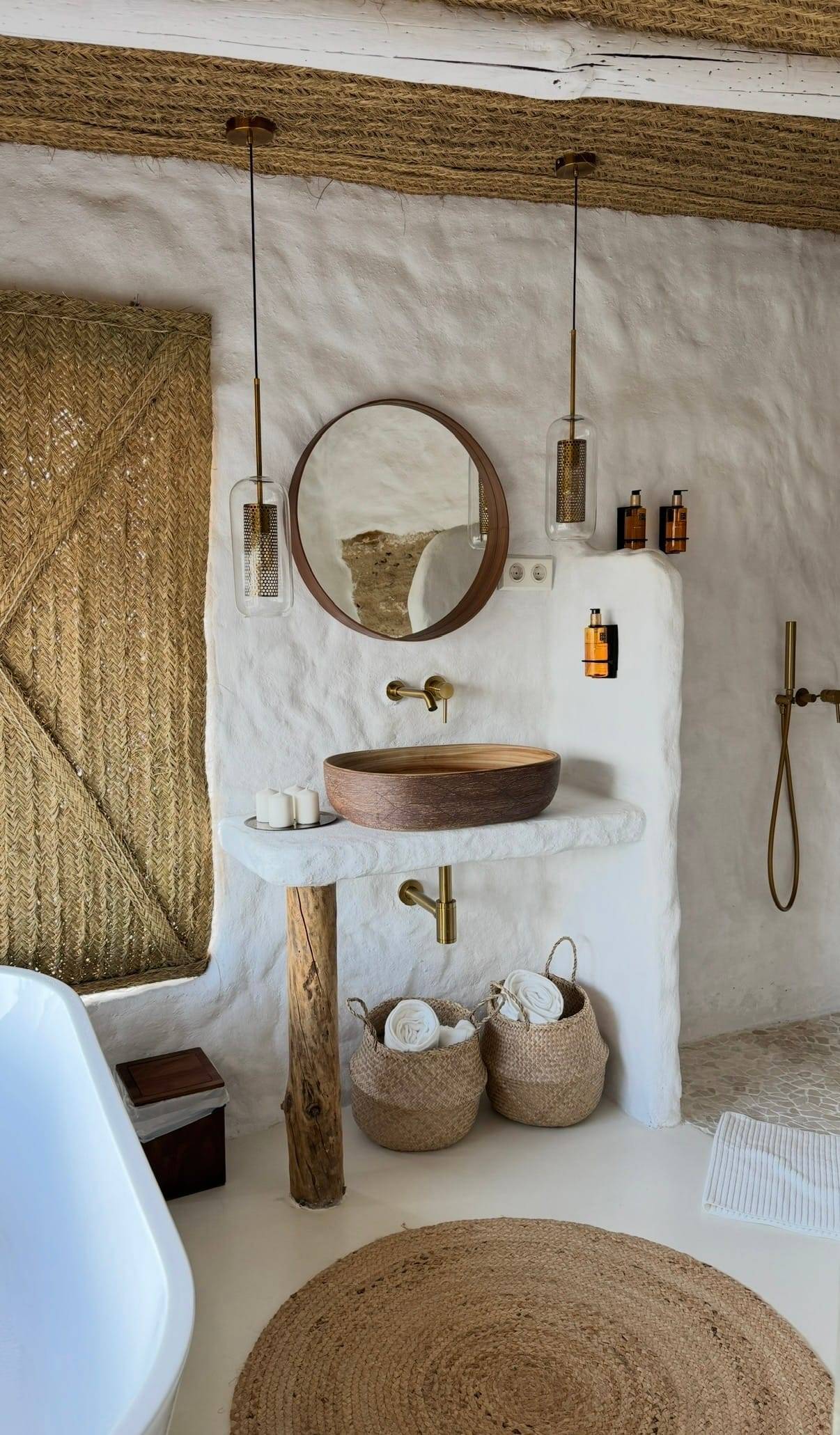Baño encalado con lavabo de madera sobre una encimera de obra, espejo redondo y luces colgantes