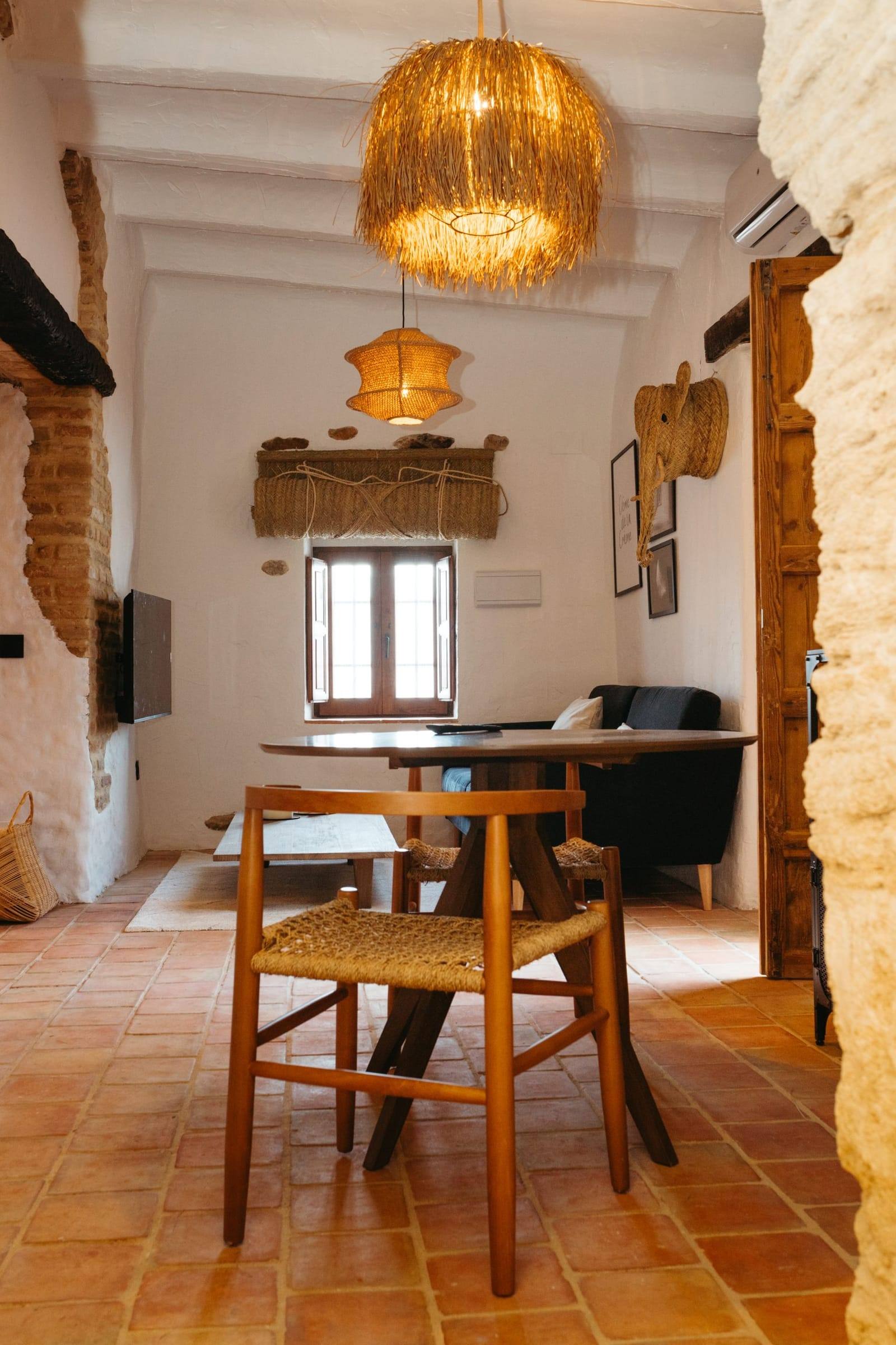 Mesa de comedor de madera con sillas de enea bajo lámparas de fibra natural