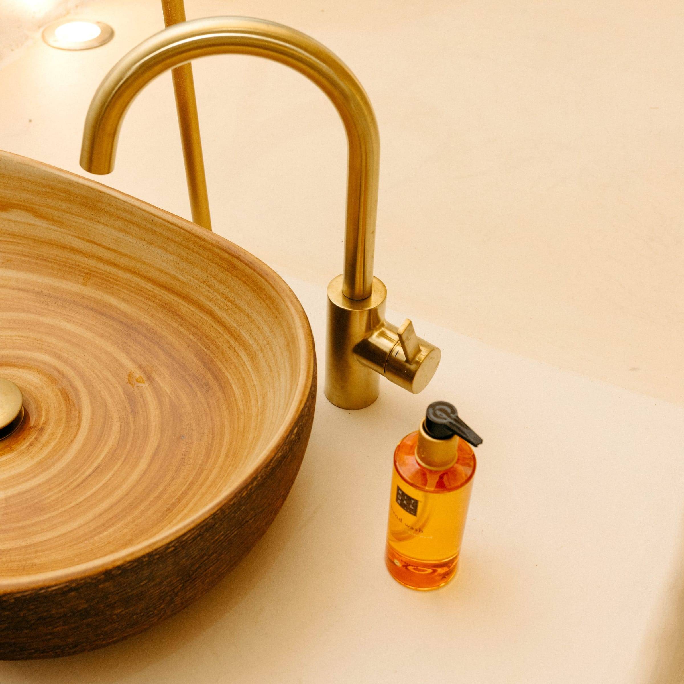Lavabo de madera torneada con grifo dorado y jabón de color ámbar