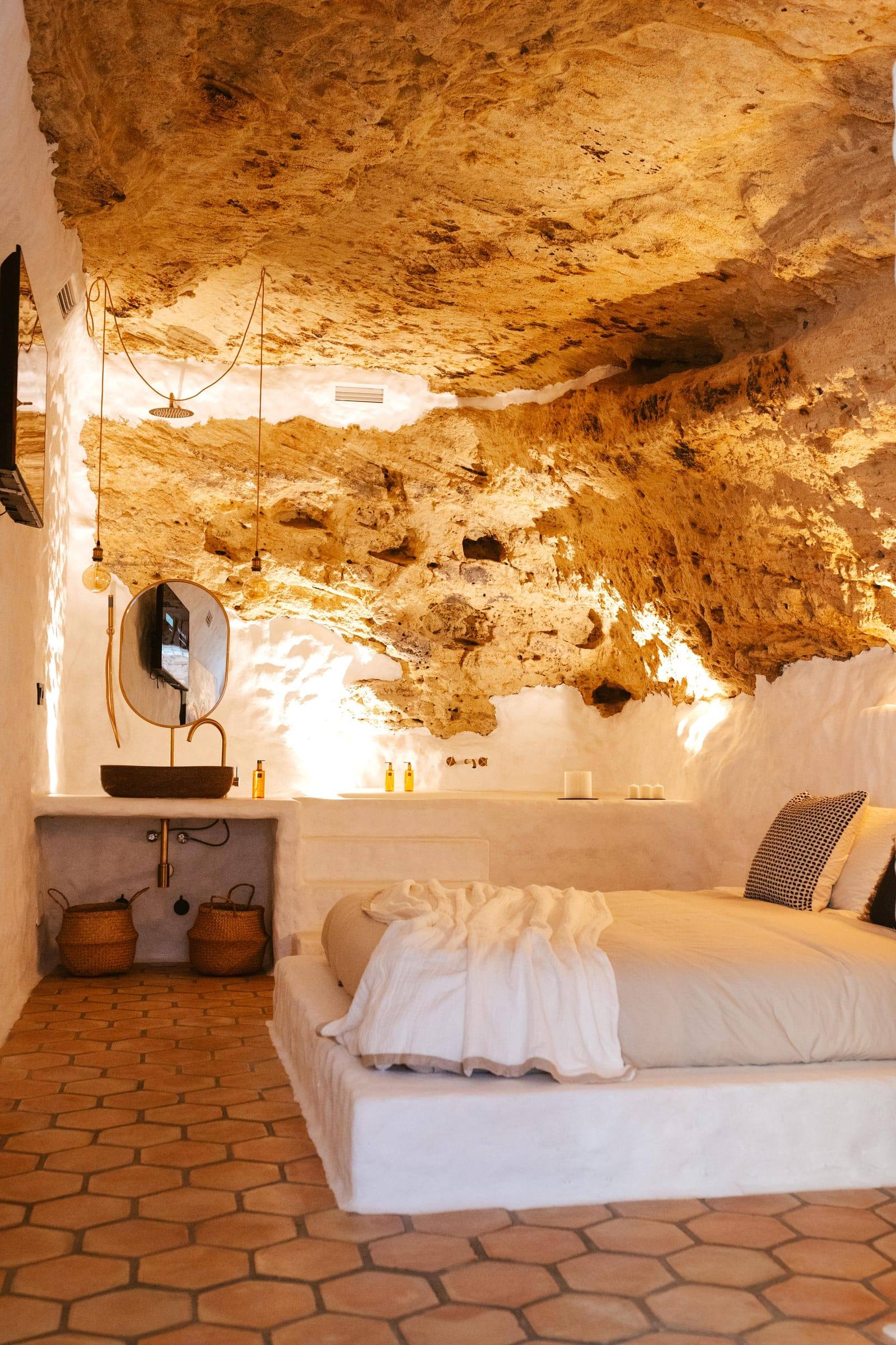 Cama de obra con ropa blanca bajo la roca iluminada, sobre suelo de barro hexagonal