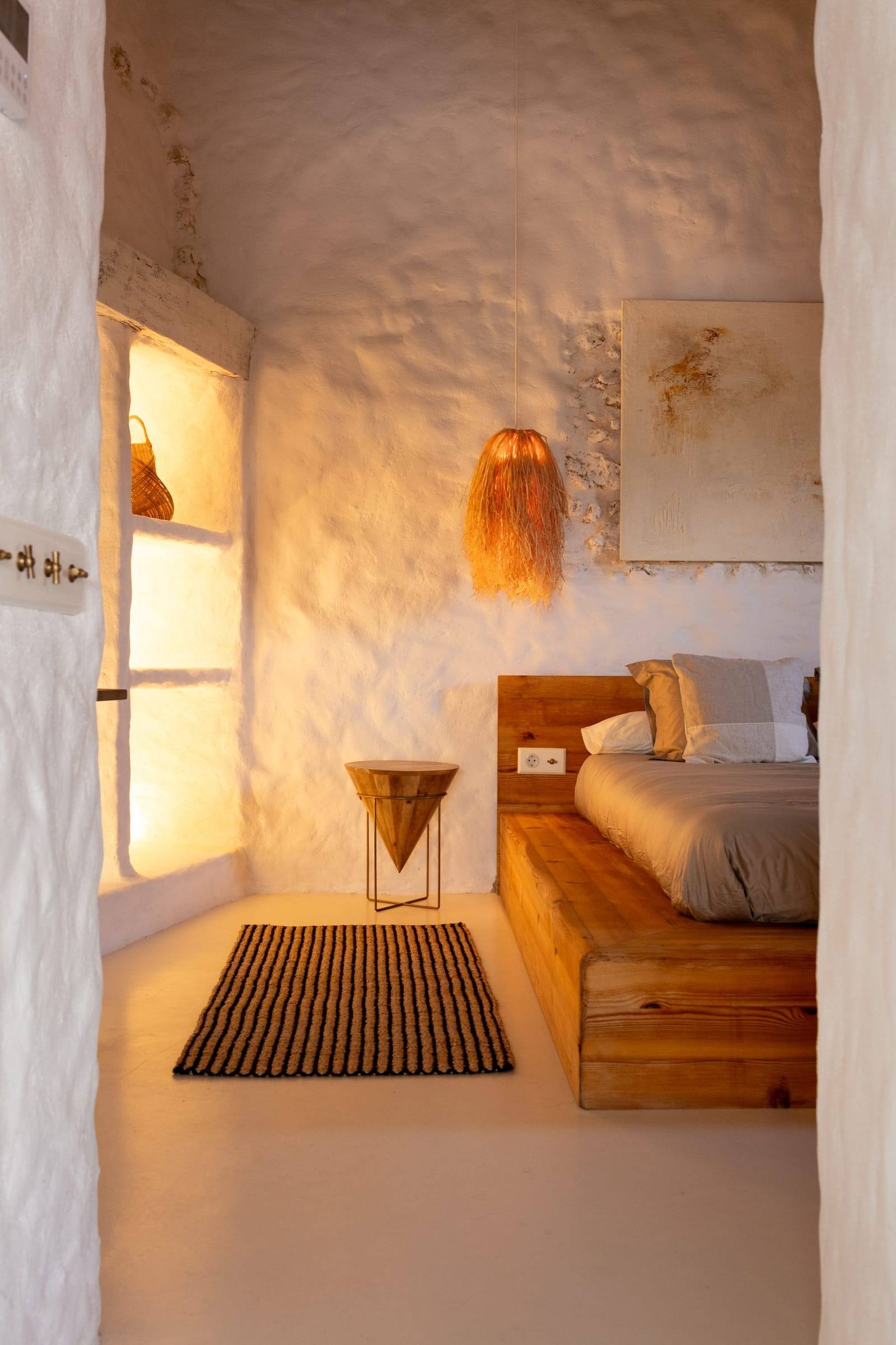 Dormitorio encalado con cama de madera, lámpara de fibra y alfombra de rayas