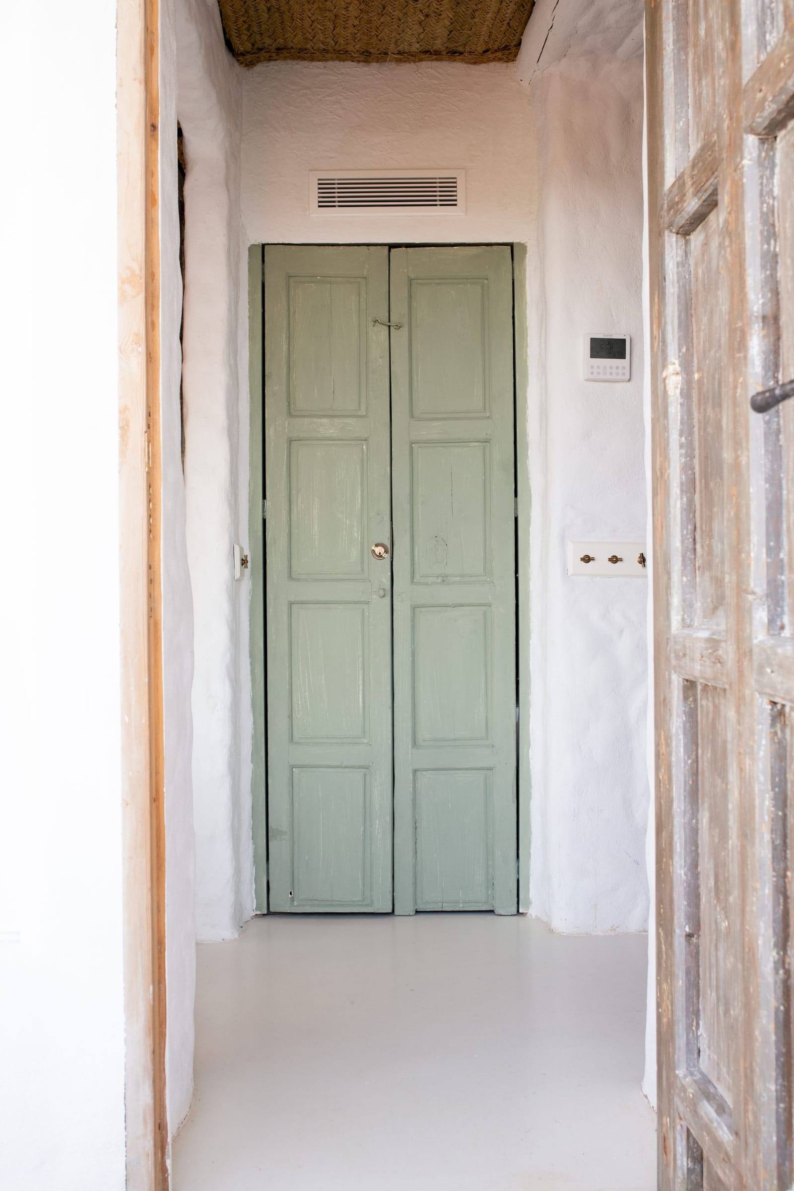 Pasillo blanco que termina en una puerta de madera pintada de verde