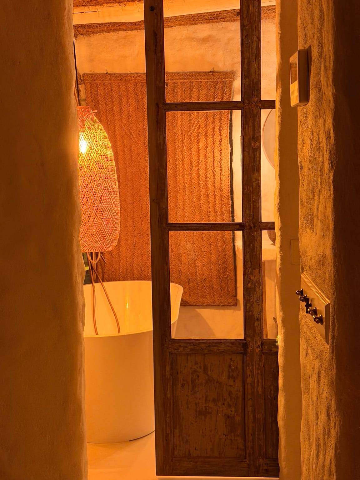 Puerta de madera y cristal entreabierta que deja ver una bañera exenta con luz cálida